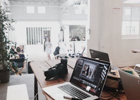 A bright, modern workspace featuring laptops, a camera, and a drawing tablet in an indoor office.